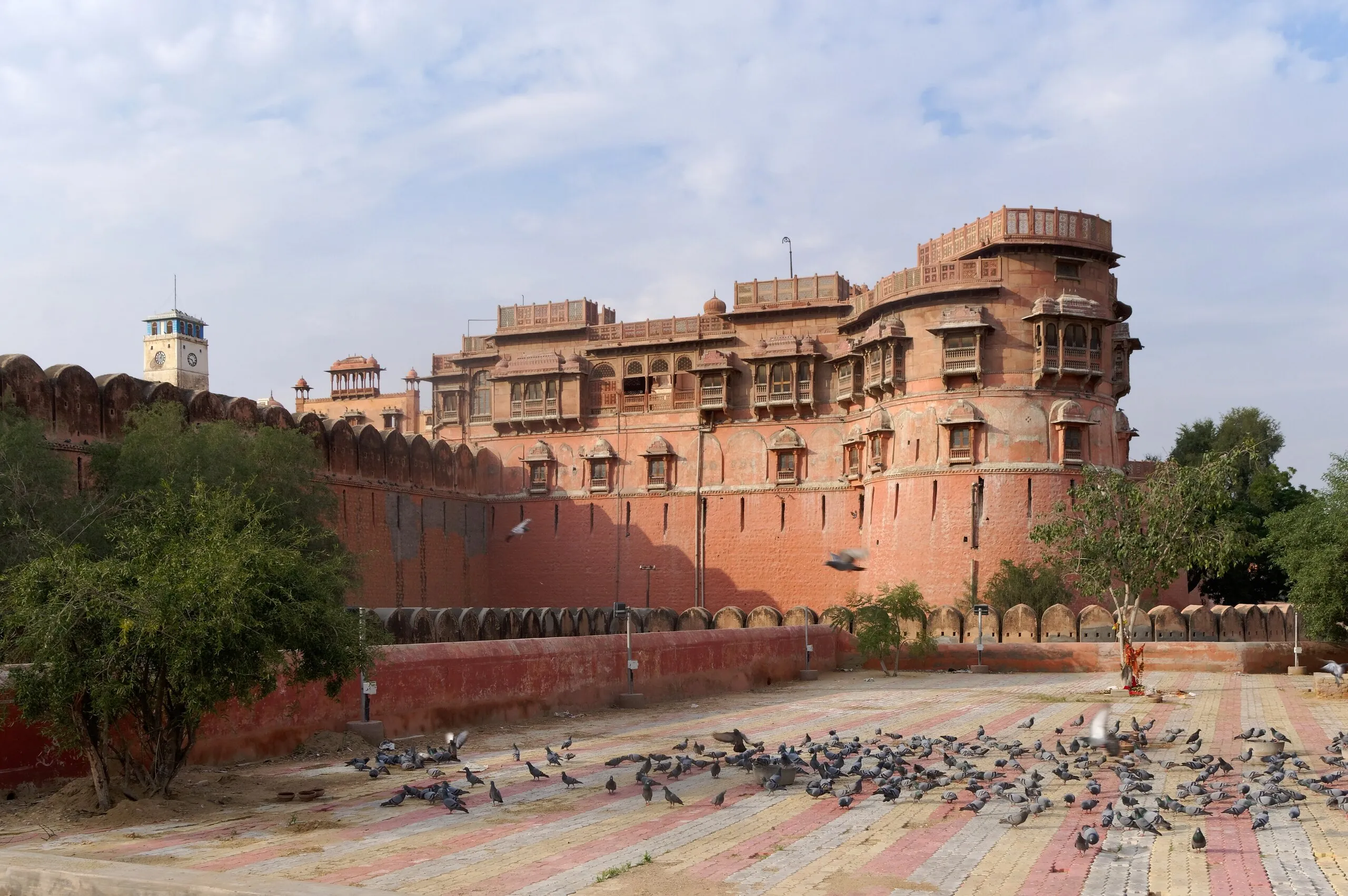 Red sandstone ramparts and balconied palace blocks of Junagarh Fort, Bikaner, above a courtyard of pigeons in afternoon light