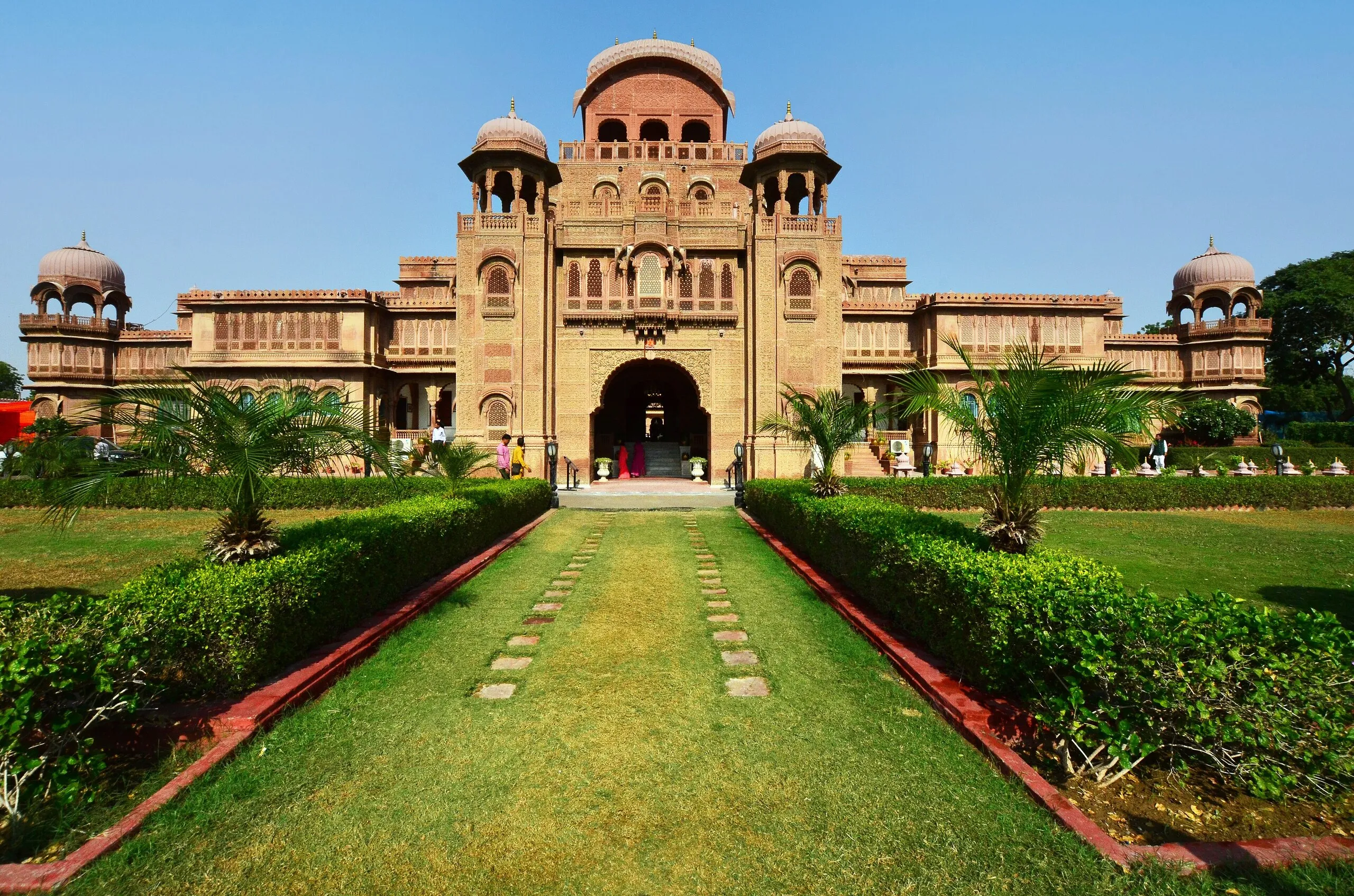Symmetrical front of Lalgarh (Laxmi Niwas) Palace in Bikaner, red sandstone domes and chhatris above a lawn path under clear sky