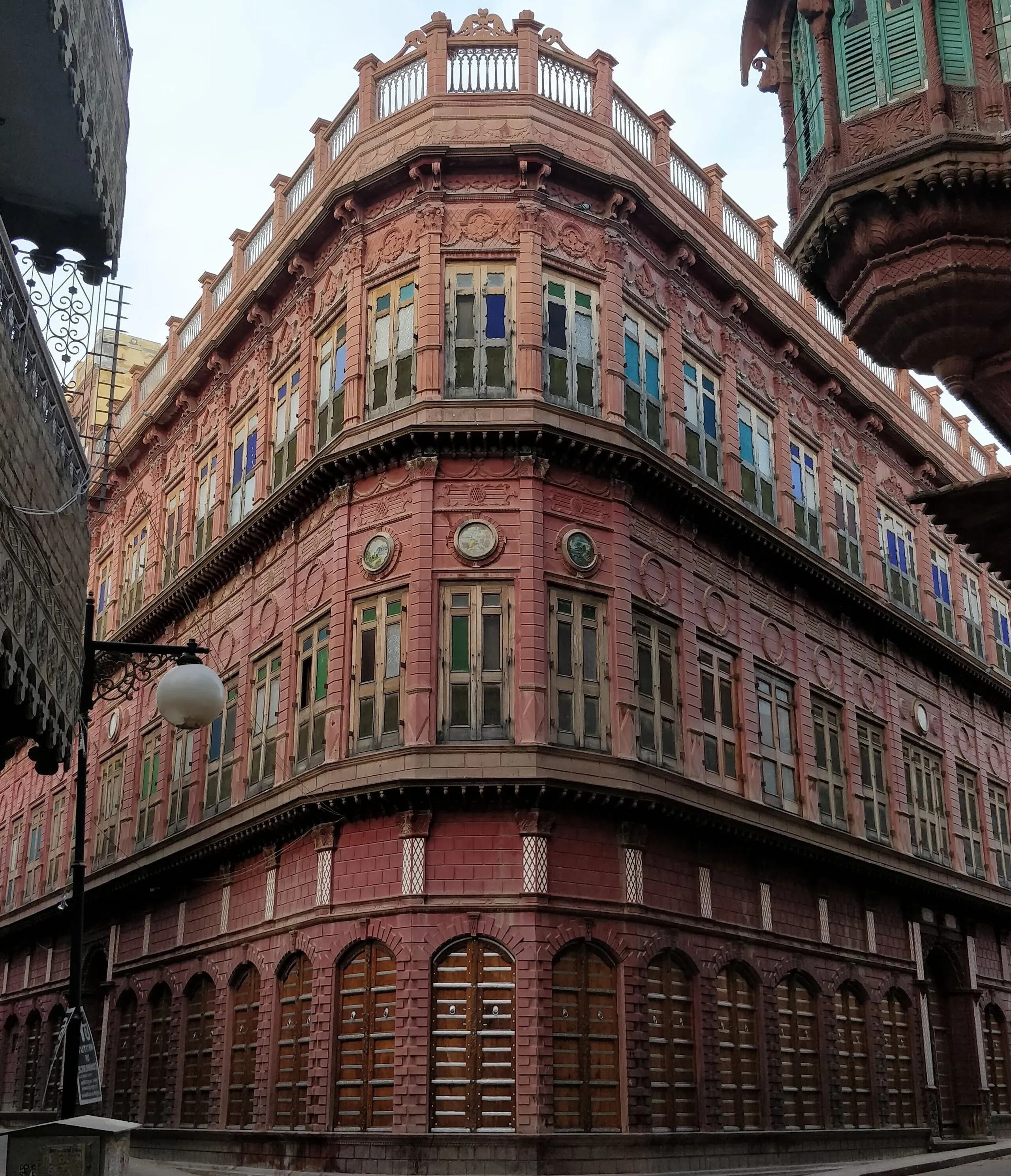 Ornate red sandstone corner facade of a Rampuriya Haveli in Bikaner, tiers of jharokha windows above arched shuttered ground floor
