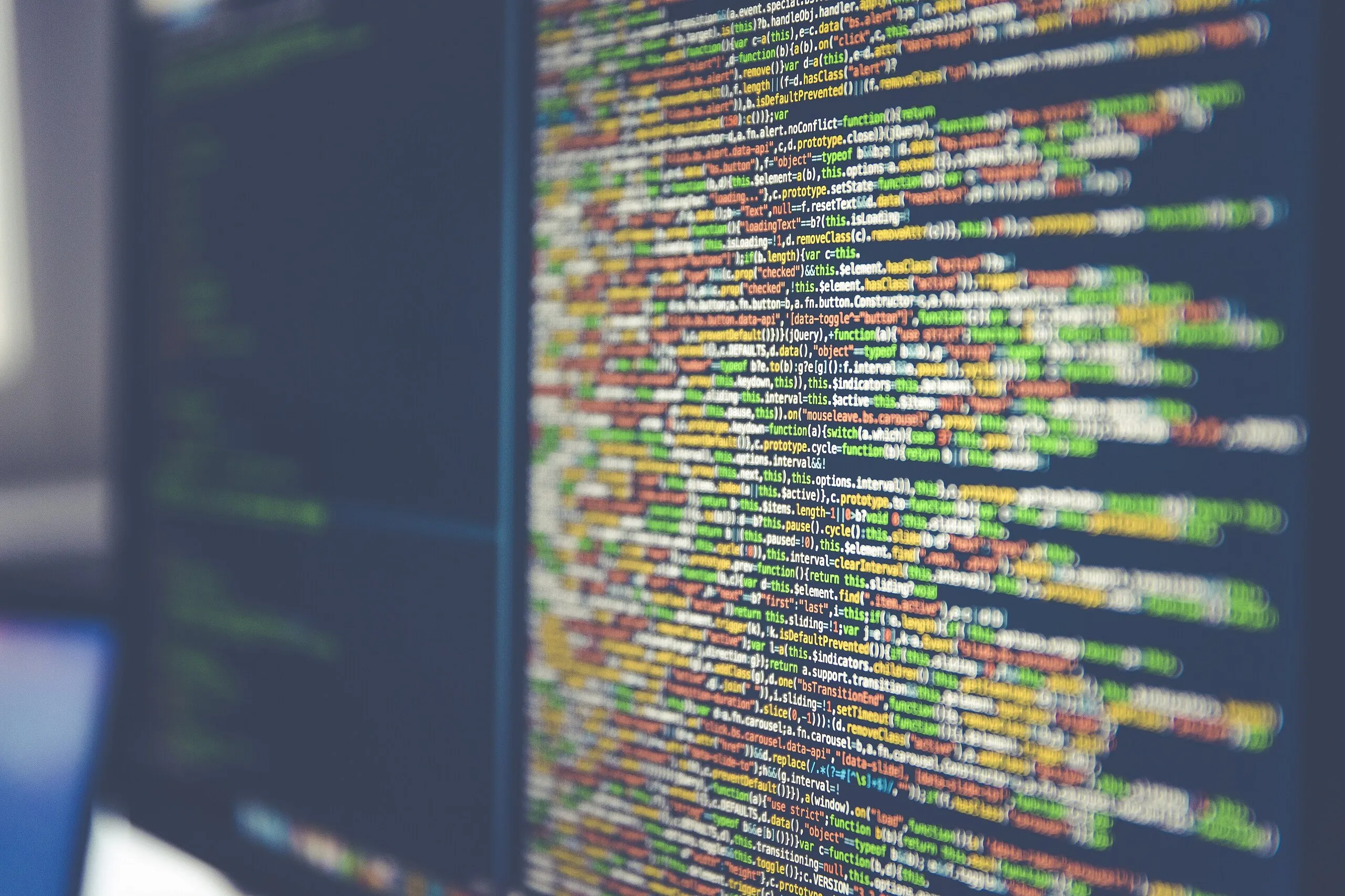 Colourful source code on a dark monitor, sharp across the centre and falling into soft focus at the edges