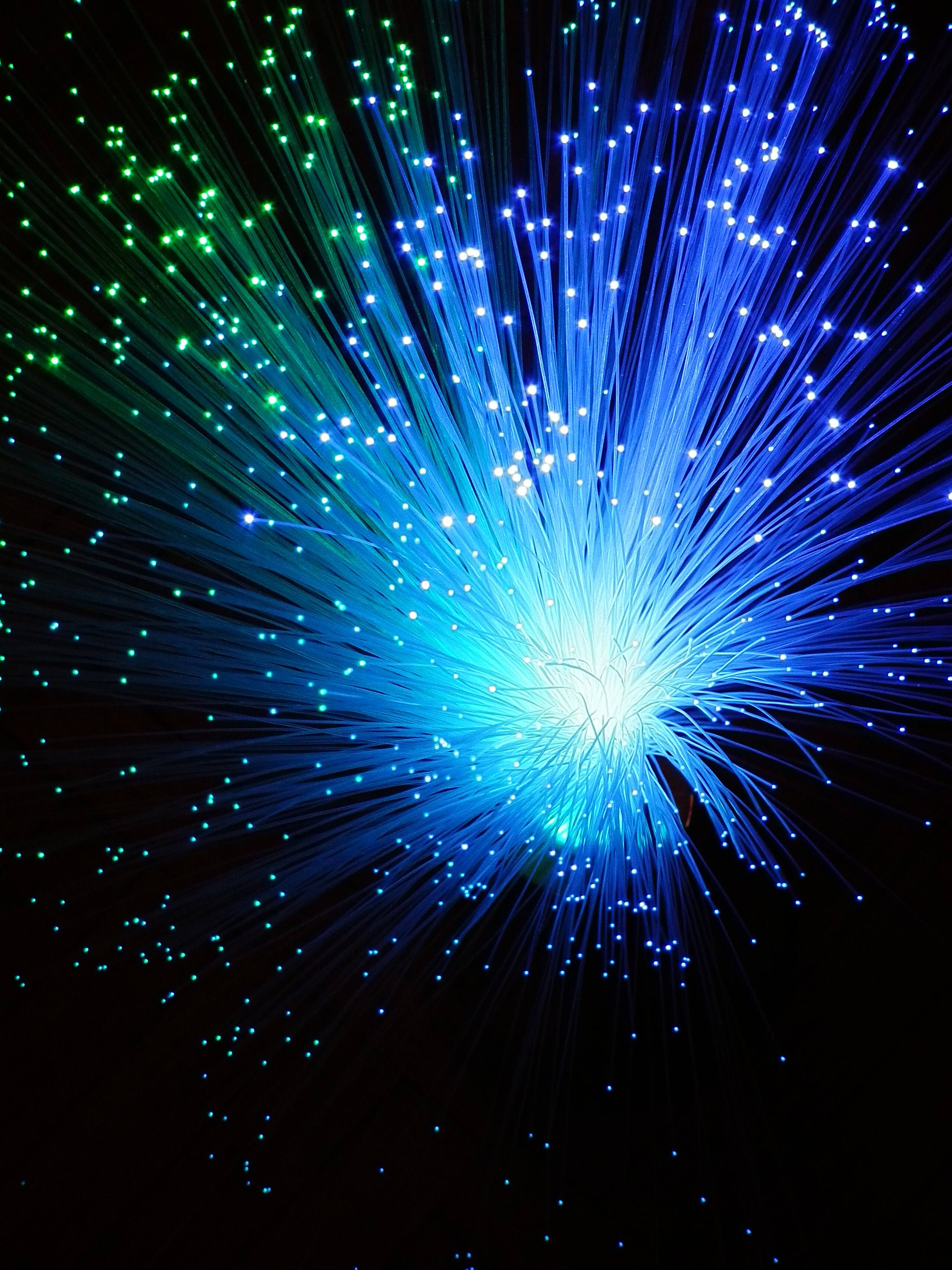 Blue and green optical-fibre strands fanning out in glowing points of light from an LED fibre lamp against black