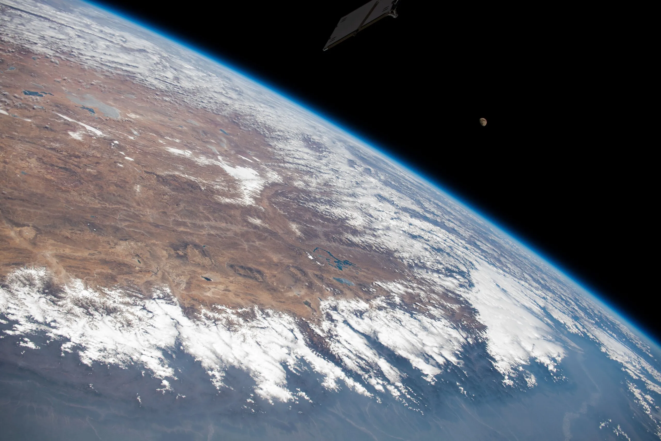 The Himalayas and the high plateau beyond curve along Earth's limb in this ISS view across India into China, the Moon above the horizon