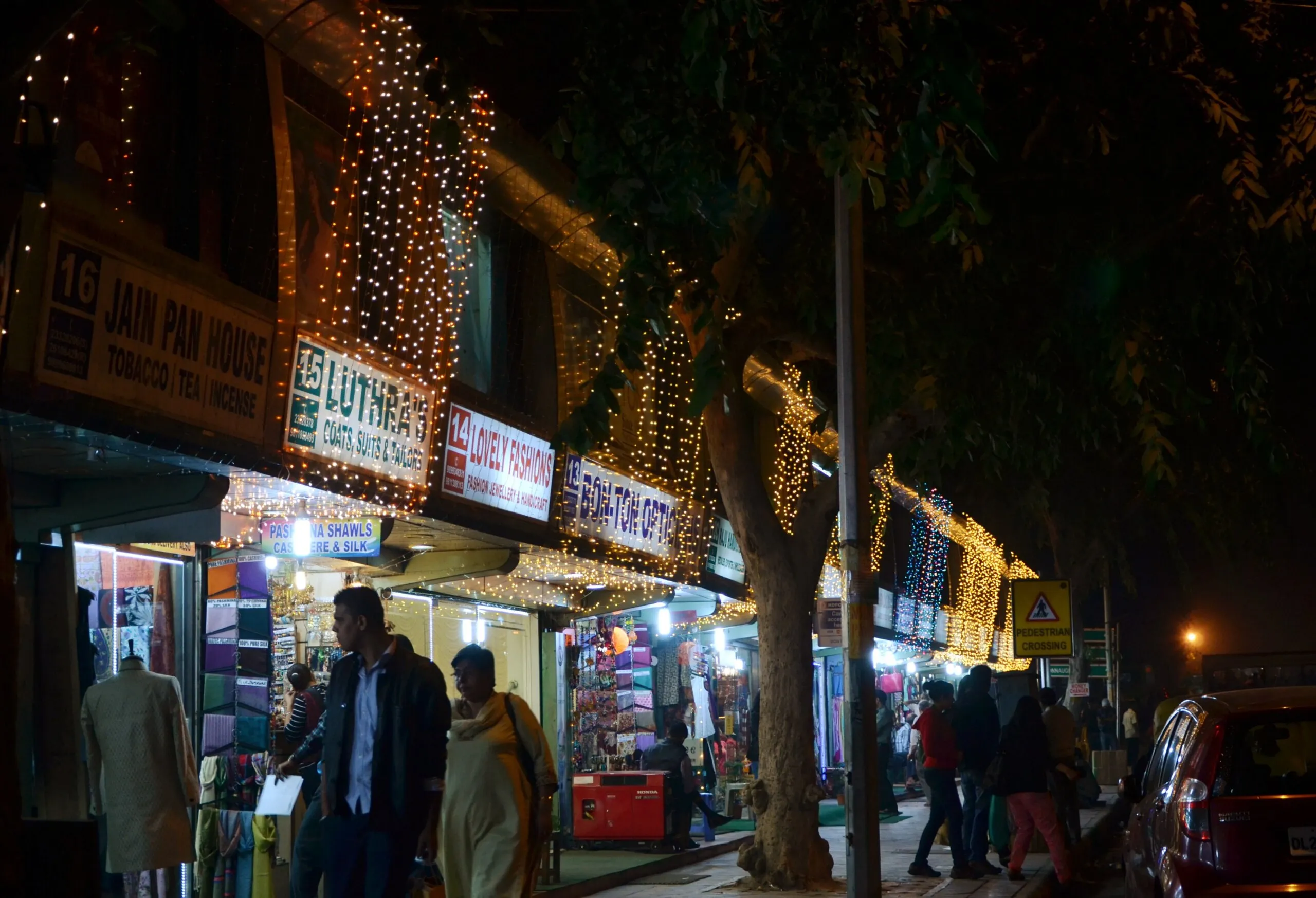 Shopfronts draped in fairy lights on Janpath, New Delhi, at night, shoppers walking beneath a tree