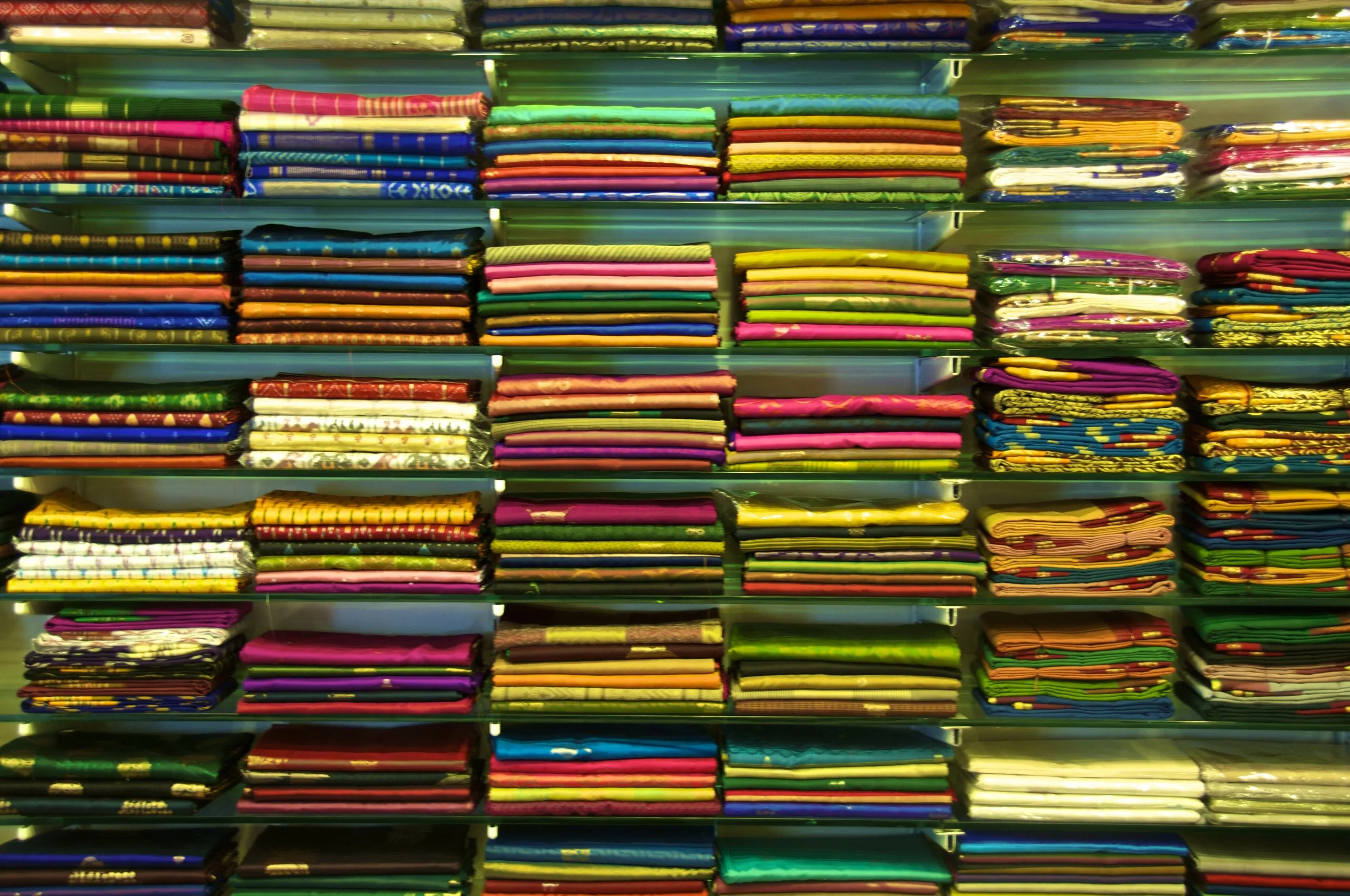 Floor-to-ceiling glass shelves of neatly folded sarees in every colour in an Indian saree shop