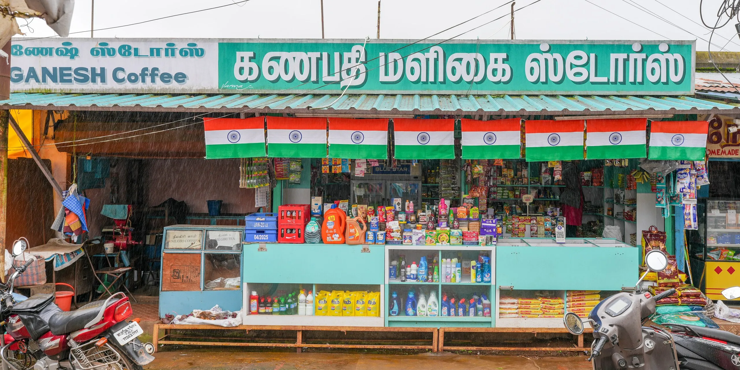 Tamil-signed provision store in Ooty Municipal Market, Tamil Nadu, with a row of Indian flags, a teal counter and packed shelves