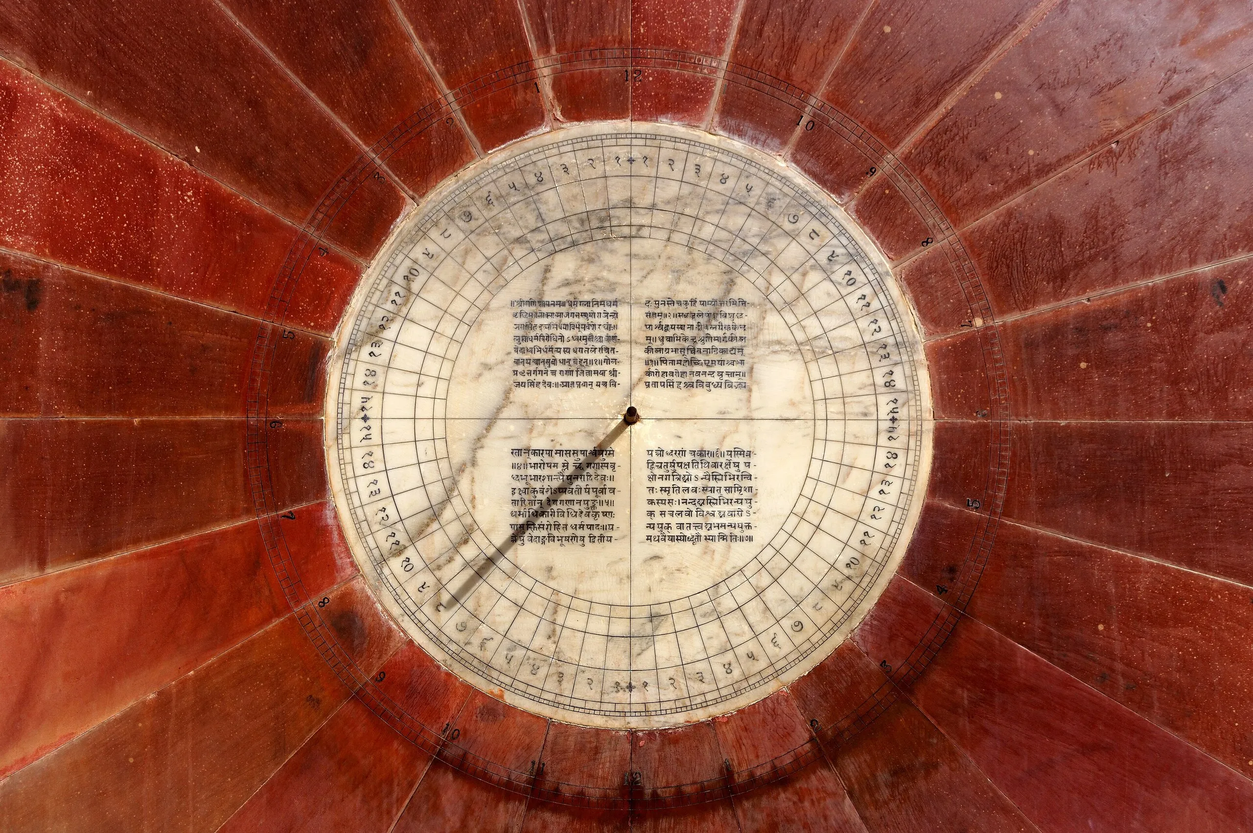Close view of a Nadivalaya Yantra sundial at Jantar Mantar, Jaipur: a marble dial with Devanagari text, ringed by red sandstone segments